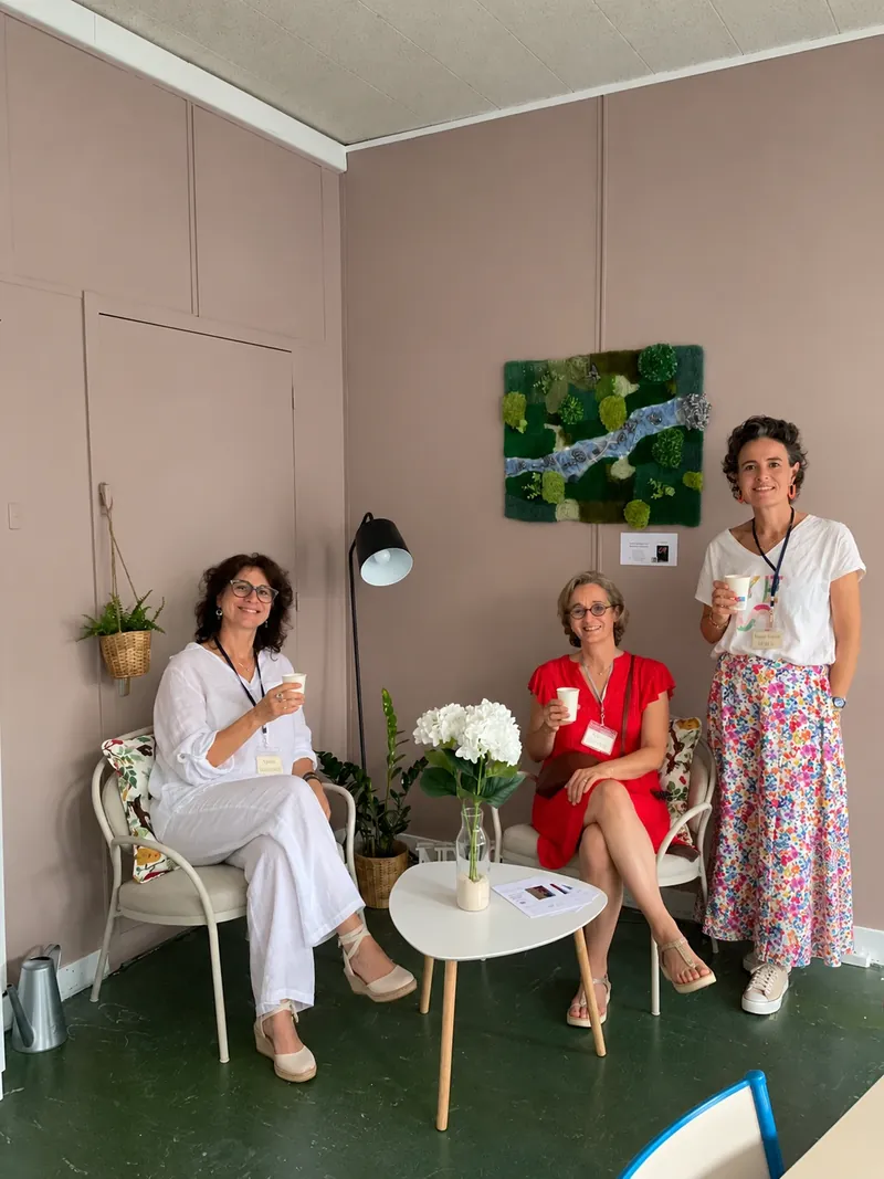 Trois personnes avec un café à la main dans un coin salon aménagé, deux assises et une debout